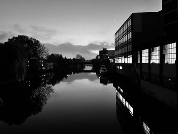 Silhouette buildings by river against sky