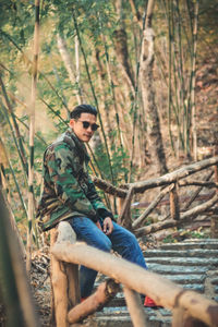 Portrait of young man sitting on tree in forest