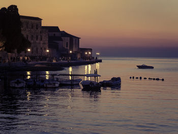 Boats in sea against illuminated buildings at sunset