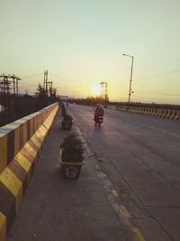 Vehicles on road against sky during sunset