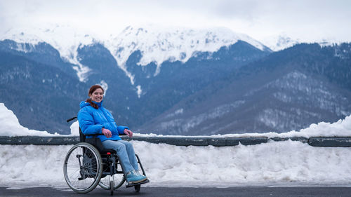 Woman sitting on wheelchair against snowcapped mountains