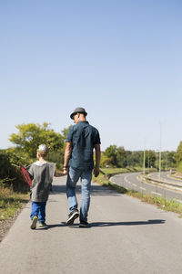 Rear view of father and son walking on road against clear sky