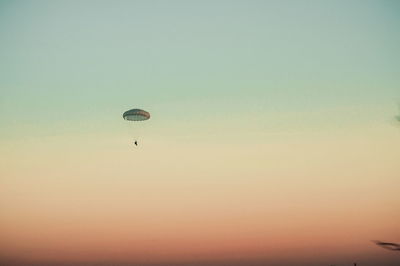 Low angle view of person paragliding against clear sky during sunset