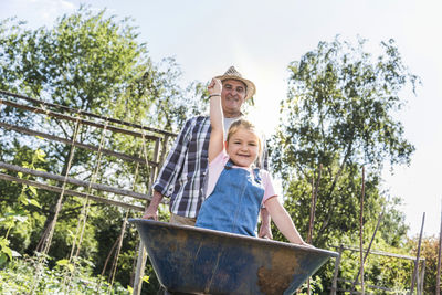 Grandfather pushing wheelbarrow with granddaughter in the garden