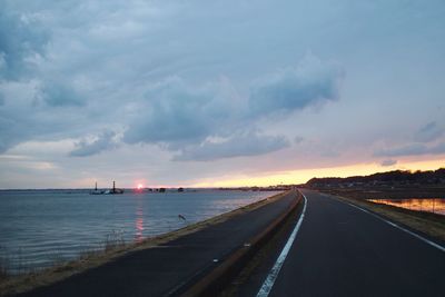 Road by sea against sky during sunset