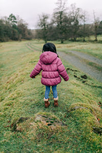 Rear view of girl in pink jacket standing on field