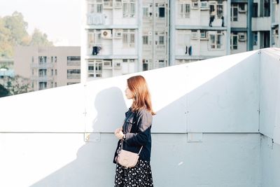 Rear view of woman with umbrella standing against buildings