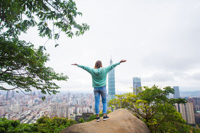 Rear view of man with arms outstretched standing against cityscape