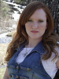 Portrait of beautiful young woman against tree trunk