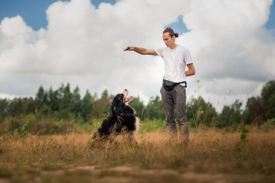 Man with dog standing on field against sky