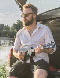 Bearded man singing while playing ukulele in car trunk