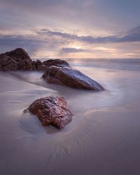 Rocks on shore against sky during sunset