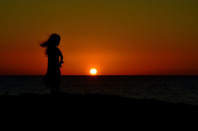 Silhouette woman standing on beach against sky during sunset