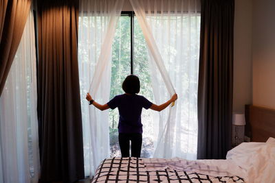 Rear view of man standing by window at home