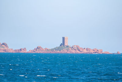 Lighthouse by sea against clear sky