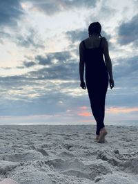 Rear view of woman standing on beach during sunset