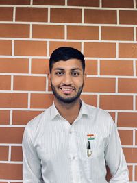 Portrait of young man standing against brick wall