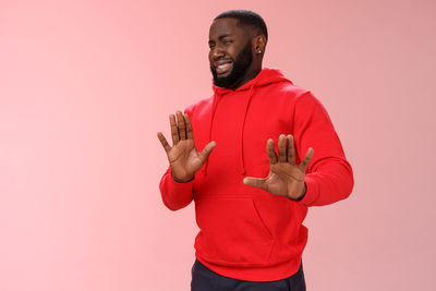 Young man standing against pink background