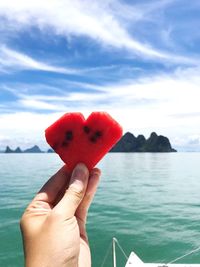 Close-up of hand holding strawberry over sea against sky