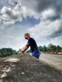 Side view of man sitting on road against sky