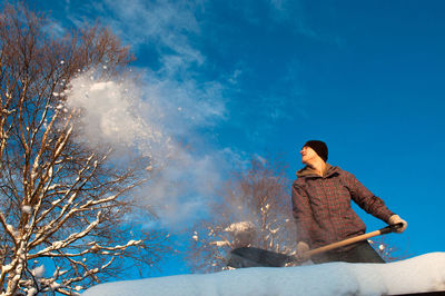 Low angle view of man throwing snow against blue sky