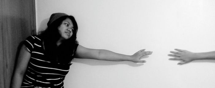 Cropped hand reaching towards woman against wall