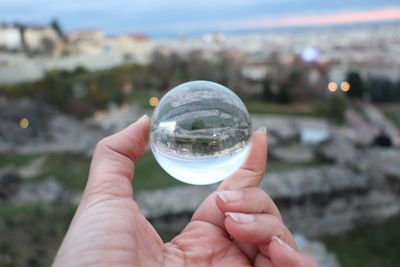 Cropped hand holding crystal ball against city