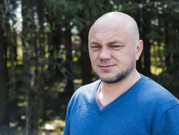 Close-up thoughtful bald man standing against trees