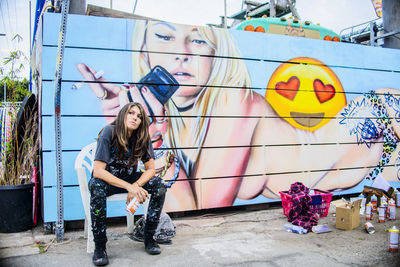 Full length portrait of young woman against graffiti wall