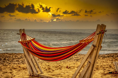 Deck chairs on beach against sky during sunset