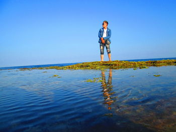 Full length of man standing in sea against clear blue sky