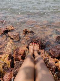 Low section of woman relaxing on rock by sea