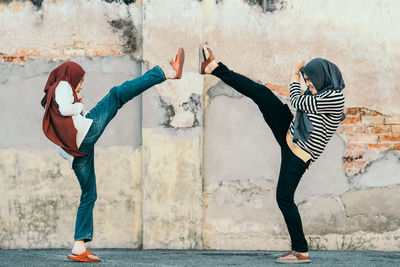 Friends kicking by weathered wall