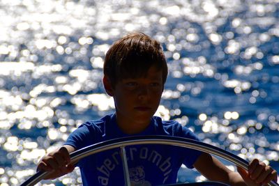 Boy steering boat against sea on sunny day