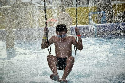 Water spraying on boy swinging over swimming pool