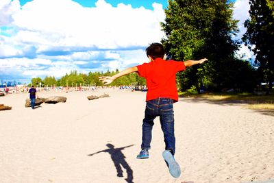 Rear view of boy playing on beach against sky