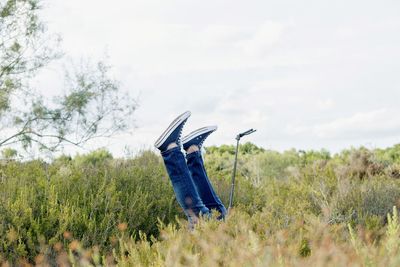 Low section of person with feet up amidst plants against sky