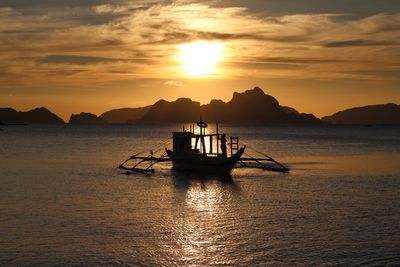 Silhouette boat sailing in sea against sky during sunset