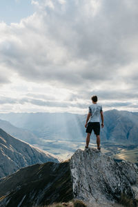 Rear view of man standing on rock against sky