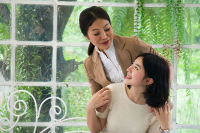 Happy mother and daughter looking each other against window