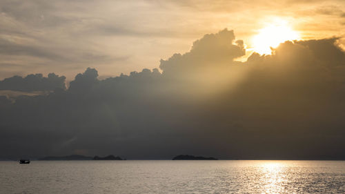 Sunlight streaming through clouds over sea during sunset