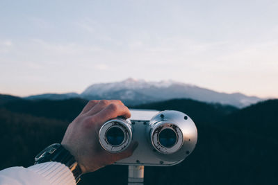 Close-up of hand holding camera against sky