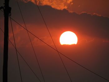 Low angle view of silhouette cables against orange sky