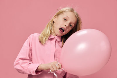 Portrait of young woman with balloons against pink background