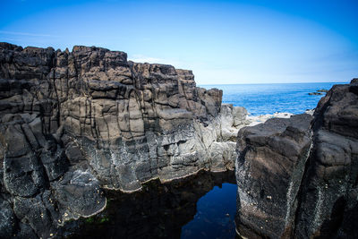 Rock formations by sea against blue sky