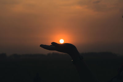 Silhouette of person holding sun during sunset