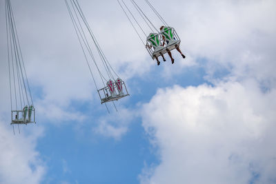 Low angle view of people sitting on amusement park ride against cloudy sky