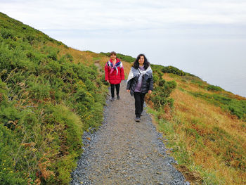 Rear view of women walking on road amidst plants against sky