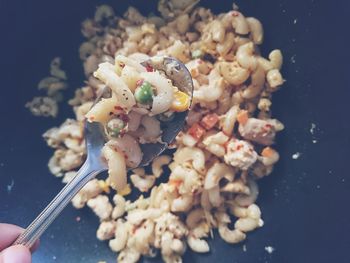 Close-up of hand holding cooked pasta in spoon