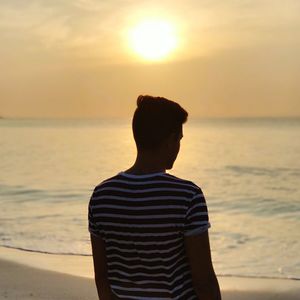 Rear view of man standing at beach during sunset